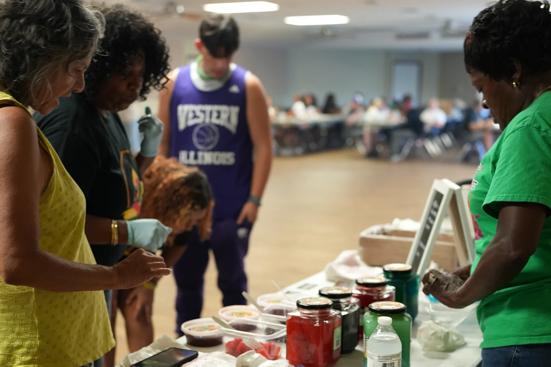 Miss Merry serving flavored pickles from her vending table at a Wichita community event, jars of every flavor lined up as customers sample